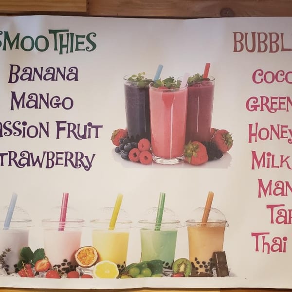 A menu board displays colorful smoothies and bubble teas with fruit garnishes and ingredient lists.