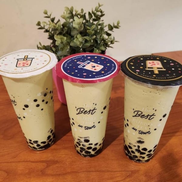 Three SaiMai Thai Restaurant bubble teas with tapioca pearls and decorative lids on a wooden table.