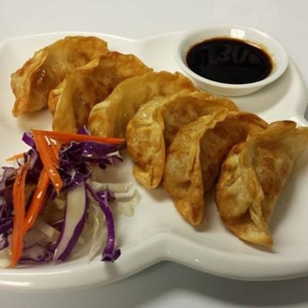 A plate of golden-brown fried dumplings with a side of shredded cabbage and carrots, and a small bowl of dark dipping sauce.